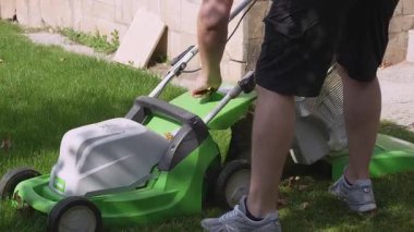 Bişkek, Kırgızistan - 09.15.2024: Bireyler, yemyeşil çimenler üzerinde elektrikli çim biçme makinesi kullanıyor, verimli bir bahçe yönetimi için tahsilat torbasını ayarlıyor