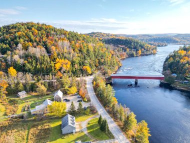 Resim, güzel bir sonbahar ormanında nehrin üzerindeki küçük kırmızı bir köprüyü gösteriyor. Ağaçlar tam yapraklı ve yapraklar sarıya, turuncuya ve kırmızıya dönüyor. Su sakin ve berrak..