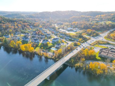 Görüntü, merkezinde bir yol olan güzel bir kırsal araziyi gösteriyor. Yol renkli sonbahar ağaçlarıyla çevrili ve arkasında beyaz bulutlar olan mavi bir gökyüzü var..
