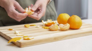 Masadaki kesme tahtasının üzerinde portakal kabuğu soyulmuş eller, Noel 'de yemek yapmak için bir sürü sulu taze meyve..