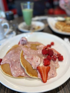 Krema, çilek ve ahududulu krep yığınının tadını çıkar. Bu lezzetli yemek kahvaltı ya da kahvaltı için mükemmel. Tatlı ve meyveli bir deneyim sunuyor..