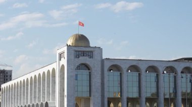 Bişkek, Kırgızistan - 09.15.2024: Altın bir kubbe ve geniş cam pencerelere sahip mimari yapı, insanlarla ve yeşilliklerle dolu, kentsel kültür ve toplumu yansıtıyor