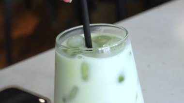 Yeşil bir kibrit sütlü sütlü kahvenin yakın çekimi. Latte üzerinde kalp şeklinde köpük tasarımı içeriyor. Arka planda bir tatlı kısmen görülebilir..