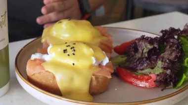 Karışık salata ve dilimlenmiş domatesle servis edilen haşlanmış yumurta ve holandez soslu bir tabak benedikt. Canlı renklerde kahvaltı..