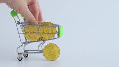 Parlak altın paralarla dolu minyatür alışveriş arabası kripto para birimini sembolize ederek dijital para birimi ve modern finansal uygulamalar kavramını temsil eder.