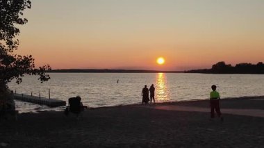 Gatineau QC, Kanada - 22 Temmuz 2025: İnsanlar plajda sakin bir gün batımına karşı gölgeli ve gökyüzünde canlı renkler var.