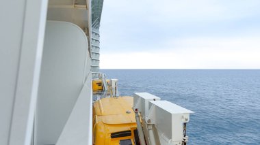 Gemi güvertesi görünümünde sakin okyanusa bakan sarı makineler ve metin için geniş kopya alanı olan bulutlu gökyüzü