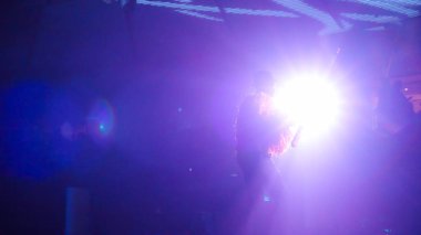 Sahnede parlak mor ışıklarla aydınlatılan bir sanatçının silueti canlı müzik performansı sırasında büyüleyici bir ortam yaratıyor.