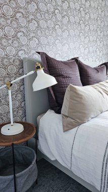 Konforlu yatak odası dekoratif yastıklar ve modern bir lambayla şık bir yatak sergileniyor. Rahatlamak ve rahatlamak için davetkar atmosferi arttırıyor.