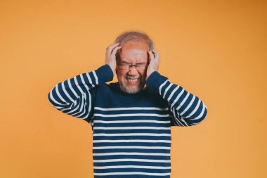 Asyalı kıdemli yaşlı adam, sarı arka planda ağrı ve migren yüzünden baş ağrısı çeken çaresiz ve stresli ellerini tutuyor..