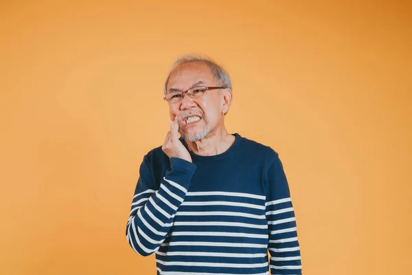 Dental pain. Portrait senior old man sad hand touching cheek suffering from toothache studio shot isolated on yellow background, Asian unhappy elder man problems with teeth pain, dental healthcare