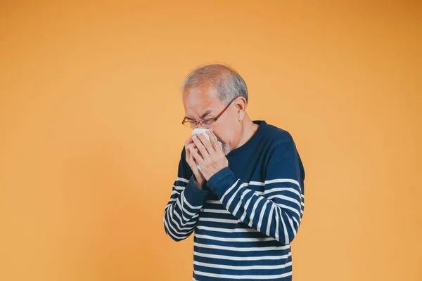 stock image Senior old man sneezing with tissue, Asian elderly man sick, cold having fever and flu sinus from sickness virus problem use tissue, pensioner unwell on the yellow background