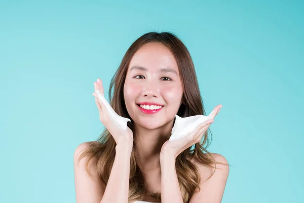 脸上的泡沫洗涤剂洗净和擦拭 快乐迷人的年轻亚洲女人在蓝色的背景上申请她的脸 — 图库照片