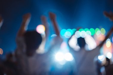 Kalabalık sahne ışıklarını yakıyor ve insanlar seyirci siluetini hayran bırakıyor. Müzik festivalinin arka planında sahne ışığı gece hayatı etkinliğiyle el kaldırıyor..