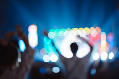 Kalabalık sahne ışıklarını yakıyor ve insanlar seyirci siluetini hayran bırakıyor. Müzik festivalinin arka planında sahne ışığı gece hayatı etkinliğiyle el kaldırıyor..