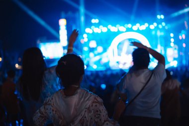 Kalabalık sahne ışıklarını yakıyor ve insanlar seyirci siluetini hayran bırakıyor. Müzik festivalinin arka planında sahne ışığı gece hayatı etkinliğiyle el kaldırıyor..
