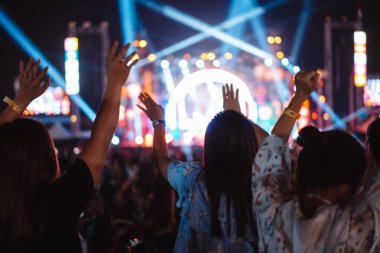 Kalabalık sahne ışıklarını yakıyor ve insanlar seyirci siluetini hayran bırakıyor. Müzik festivalinin arka planında sahne ışığı gece hayatı etkinliğiyle el kaldırıyor..