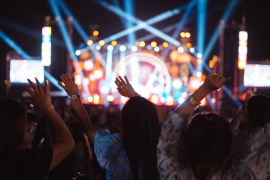 Kalabalık sahne ışıklarını yakıyor ve insanlar seyirci siluetini hayran bırakıyor. Müzik festivalinin arka planında sahne ışığı gece hayatı etkinliğiyle el kaldırıyor..