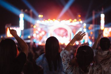Kalabalık sahne ışıklarını yakıyor ve insanlar seyirci siluetini hayran bırakıyor. Müzik festivalinin arka planında sahne ışığı gece hayatı etkinliğiyle el kaldırıyor..