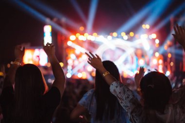 Kalabalık sahne ışıklarını yakıyor ve insanlar seyirci siluetini hayran bırakıyor. Müzik festivalinin arka planında sahne ışığı gece hayatı etkinliğiyle el kaldırıyor..