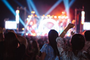 Kalabalık sahne ışıklarını yakıyor ve insanlar seyirci siluetini hayran bırakıyor. Müzik festivalinin arka planında sahne ışığı gece hayatı etkinliğiyle el kaldırıyor..