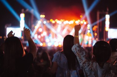 Kalabalık sahne ışıklarını yakıyor ve insanlar seyirci siluetini hayran bırakıyor. Müzik festivalinin arka planında sahne ışığı gece hayatı etkinliğiyle el kaldırıyor..