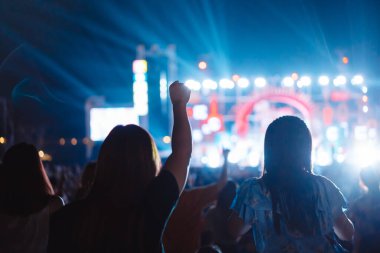 Kalabalık sahne ışıklarını yakıyor ve insanlar seyirci siluetini hayran bırakıyor. Müzik festivalinin arka planında sahne ışığı gece hayatı etkinliğiyle el kaldırıyor..