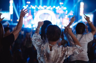 Kalabalık sahne ışıklarını yakıyor ve insanlar seyirci siluetini hayran bırakıyor. Müzik festivalinin arka planında sahne ışığı gece hayatı etkinliğiyle el kaldırıyor..