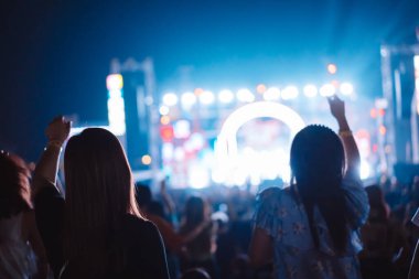Kalabalık sahne ışıklarını yakıyor ve insanlar seyirci siluetini hayran bırakıyor. Müzik festivalinin arka planında sahne ışığı gece hayatı etkinliğiyle el kaldırıyor..