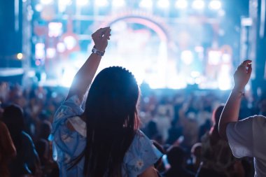 Kalabalık sahne ışıklarını yakıyor ve insanlar seyirci siluetini hayran bırakıyor. Müzik festivalinin arka planında sahne ışığı gece hayatı etkinliğiyle el kaldırıyor..