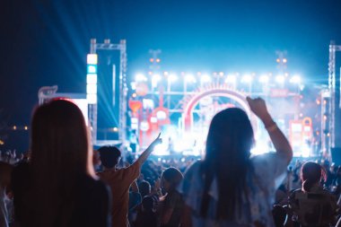 Kalabalık sahne ışıklarını yakıyor ve insanlar seyirci siluetini hayran bırakıyor. Müzik festivalinin arka planında sahne ışığı gece hayatı etkinliğiyle el kaldırıyor..