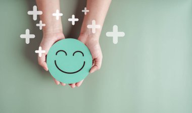 Ellerinde yeşil gülen surat, iyi geri bildirim notu, olumlu müşteri değerlendirmesi, deneyim, tatmin anketi, gülümseyen akıl sağlığı, çocuk sağlığı, yeşil arka planda dünya ruh sağlığı günü