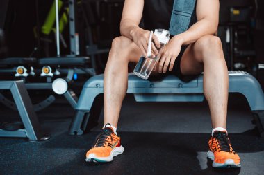 Spor salonunda egzersiz yapmak, spor yaptıktan sonra dambıl ve su şişesiyle dinlenmek sağlıklı bir vücut geliştirme..