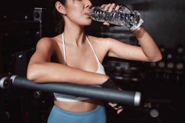 Spor salonunda su iyileştirme egzersizi yapan kadın. Kettlebell, dambıl ve su şişesiyle spor yaptıktan sonra dinleniyor. Sağlıklı vücut geliştirme..