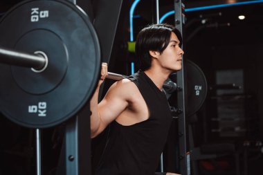 Spor salonunda ağırlık kaldıran vücut geliştirici bir adam. Vücut geliştirici halterle egzersiz yapıyor. Spor eğitimi, sağlıklı vücut geliştirme, sporcu kaslı yaşam tarzı..