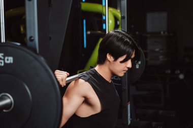 Spor salonunda ağırlık kaldıran vücut geliştirici bir adam. Vücut geliştirici halterle egzersiz yapıyor. Spor eğitimi, sağlıklı vücut geliştirme, sporcu kaslı yaşam tarzı..