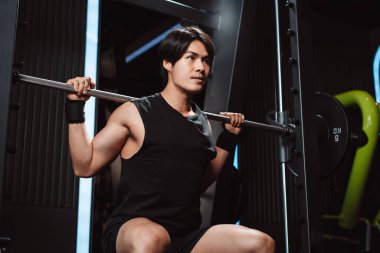 Spor salonunda ağırlık kaldıran vücut geliştirici bir adam. Vücut geliştirici halterle egzersiz yapıyor. Spor eğitimi, sağlıklı vücut geliştirme, sporcu kaslı yaşam tarzı..