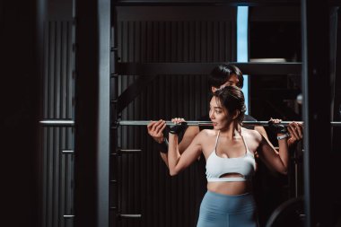 Vücut geliştiren kadın spor salonunda ağırlık kaldırmak için antrenörlük yapıyor. Vücut geliştirici halterle egzersiz yapıyor. spor eğitimi sağlıklı vücut geliştirme.