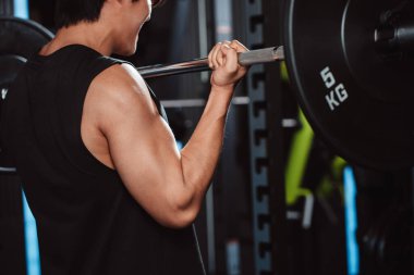 Spor salonunda halterle vücut geliştiren bir erkek. Halterle egzersiz yapan bir vücut geliştirici. Spor eğitimi, sağlıklı vücut geliştirme, sporcu kaslı yaşam tarzı..