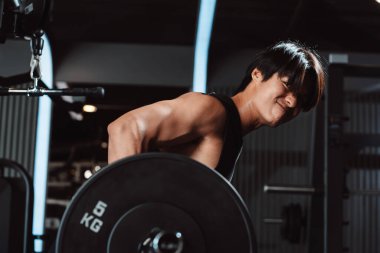 Spor salonunda halterle vücut geliştiren bir erkek. Halterle egzersiz yapan bir vücut geliştirici. Spor eğitimi, sağlıklı vücut geliştirme, sporcu kaslı yaşam tarzı..