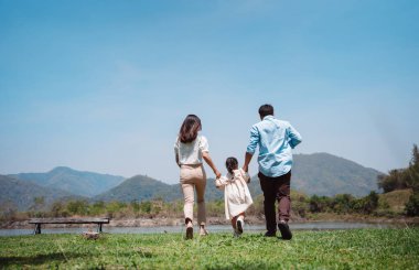 Doğa yolculuğunda mutlu bir aile. Aile hafta sonu çayırda birlikte oynuyorlardı.Nehir kenarındaki ebeveynler çocuk ve kızın ellerini tutuyorlar. Sağlık hayat sigortası konsepti.