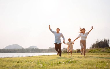 Parkta gün batımında mutlu bir aile. Aile hafta sonu çayırda birlikte koşarken nehir aileleri çocuğun elini tutuyor. Sağlık sigortası kavramı..