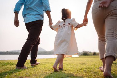 Parkta gün batımında mutlu bir aile. Aile hafta sonu çayırda birlikte koşarken nehir aileleri çocuğun elini tutuyor. Sağlık sigortası kavramı..