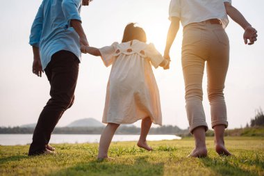Parkta gün batımında mutlu bir aile. Aile hafta sonu çayırda birlikte koşarken nehir aileleri çocuğun elini tutuyor. Sağlık sigortası kavramı..