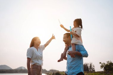 Parkta gün batımında mutlu bir aile. Aile hafta sonu çayırda birlikte koşarken nehir aileleri çocuğun elini tutuyor. Sağlık sigortası kavramı..