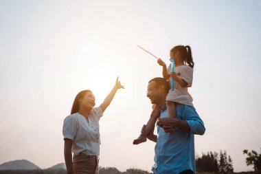 Parkta gün batımında mutlu bir aile. Aile hafta sonu çayırda birlikte koşarken nehir aileleri çocuğun elini tutuyor. Sağlık sigortası kavramı..