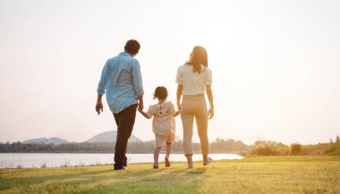 Parkta gün batımında mutlu bir aile. Aile hafta sonu çayırda birlikte koşarken nehir aileleri çocuğun elini tutuyor. Sağlık sigortası kavramı..