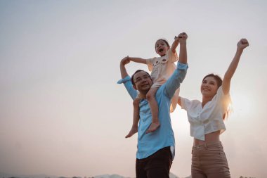 Parkta gün batımında mutlu bir aile. Aile hafta sonu çayırda birlikte koşarken nehir aileleri çocuğun elini tutuyor. Sağlık sigortası kavramı..