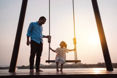 Mutlu aile gün batımında parkta salıncakla eğleniyor doğada, aile hayatının hafta sonu aktiviteleri..