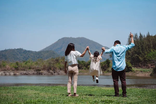 Doğa yolculuğunda mutlu bir aile. Aile hafta sonu çayırda birlikte oynuyorlardı.Nehir kenarındaki ebeveynler çocuk ve kızın ellerini tutuyorlar. Sağlık hayat sigortası konsepti.